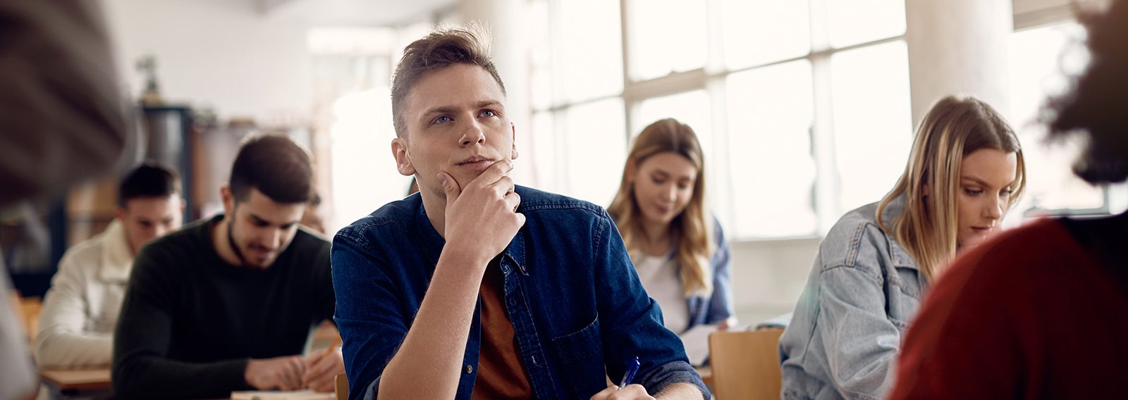 A male student looks deep in thought in a class setting surrounded by other students