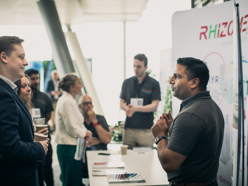 Two men talk at the Rhizome Energy stand in 2024